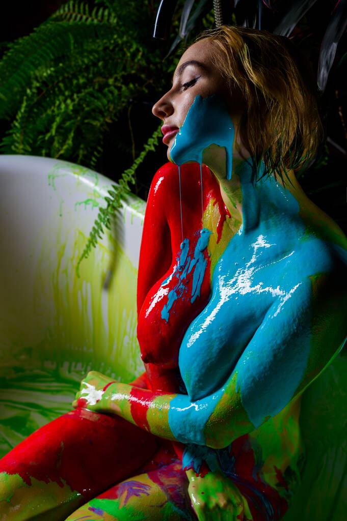 Beautiful woman posing naked in the bathroom against the background of houseplants. On the naked body of a female, streaks of paint flow down. Body painting on a girl body. - Photo, Image