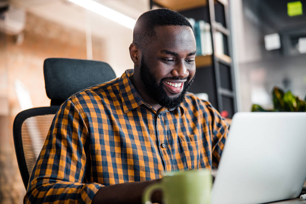 Pozitív boldog sötét bőrű férfi bámulja a laptopját - Fotó, kép