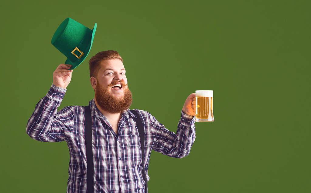 Happy St. Patricks Day. Fat man in a green hat holds his hands up glasses with beer - 写真・画像