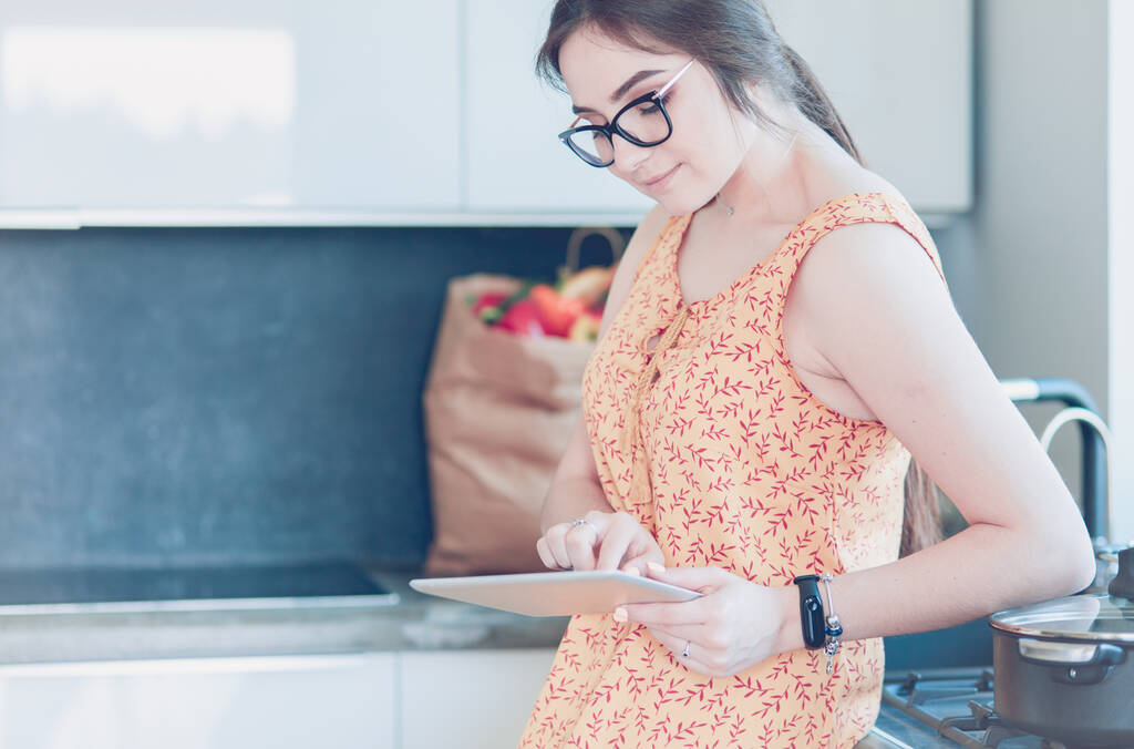 όμορφη νεαρή γυναίκα χρησιμοποιώντας ένα ψηφιακό tablet στην κουζίνα - Φωτογραφία, εικόνα