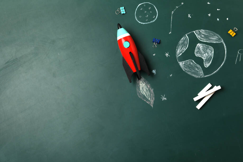 Яркая игрушечная ракета, школьные принадлежности и рисунки на доске, плоский уголок. Пространство для текста
 - Фото, изображение
