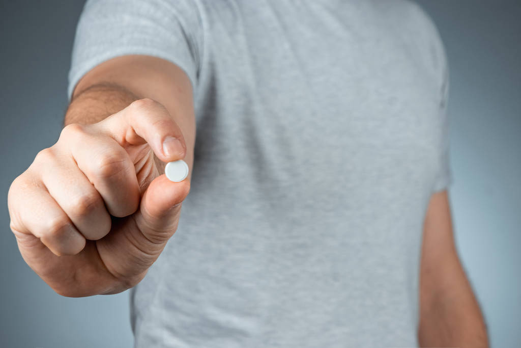Gros plan mains masculines tenant une pilule blanche, prenant des médicaments, un traitement, fond gris. Thème médical, vitamines, soins de santé
. - Photo, image