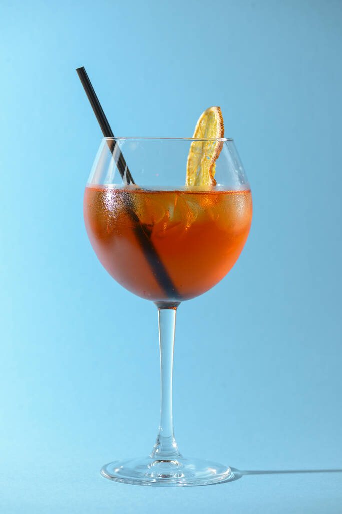 ein Glas Obstlikör im Weinglas mit einem Stück Zitrone und schwarzem Plastikstroh isoliert auf pastellblauem Hintergrund. - Foto, Bild