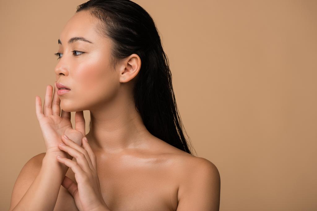 kaunis alaston aasialainen tyttö etsii pois ja koskettaa kasvot eristetty beige
 - Valokuva, kuva