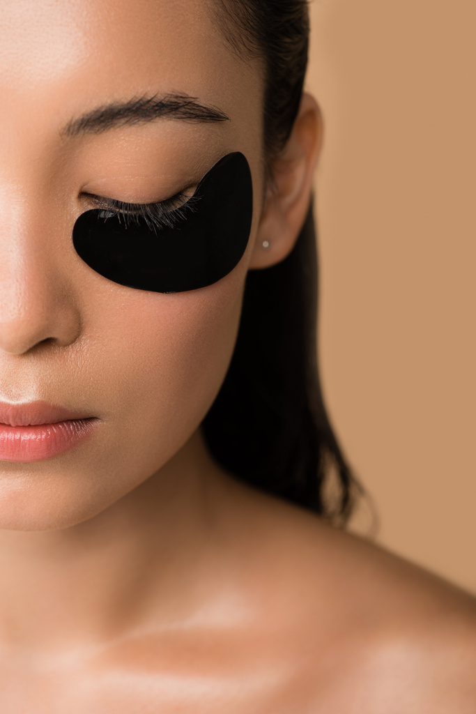 cropped view of beautiful naked asian girl with black hydrogel eye patch under closed eye isolated on beige - Photo, Image