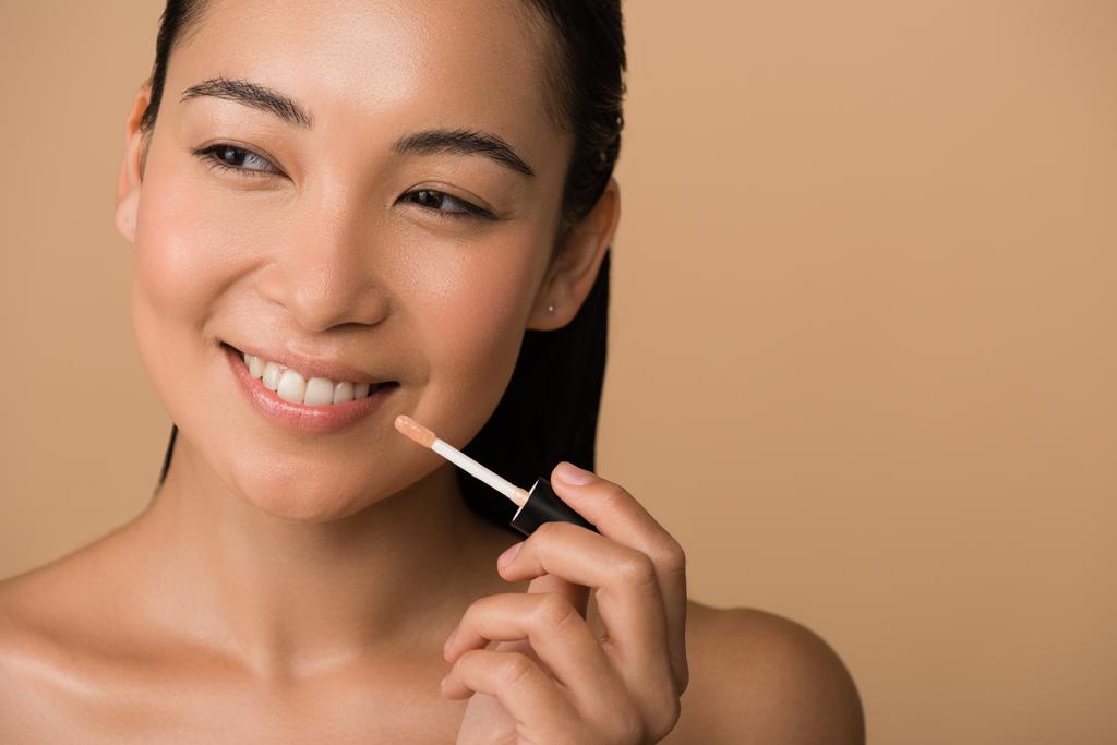 glimlachen mooi naakt aziatisch meisje appying lip gloss op lippen geïsoleerd op beige - Foto, afbeelding