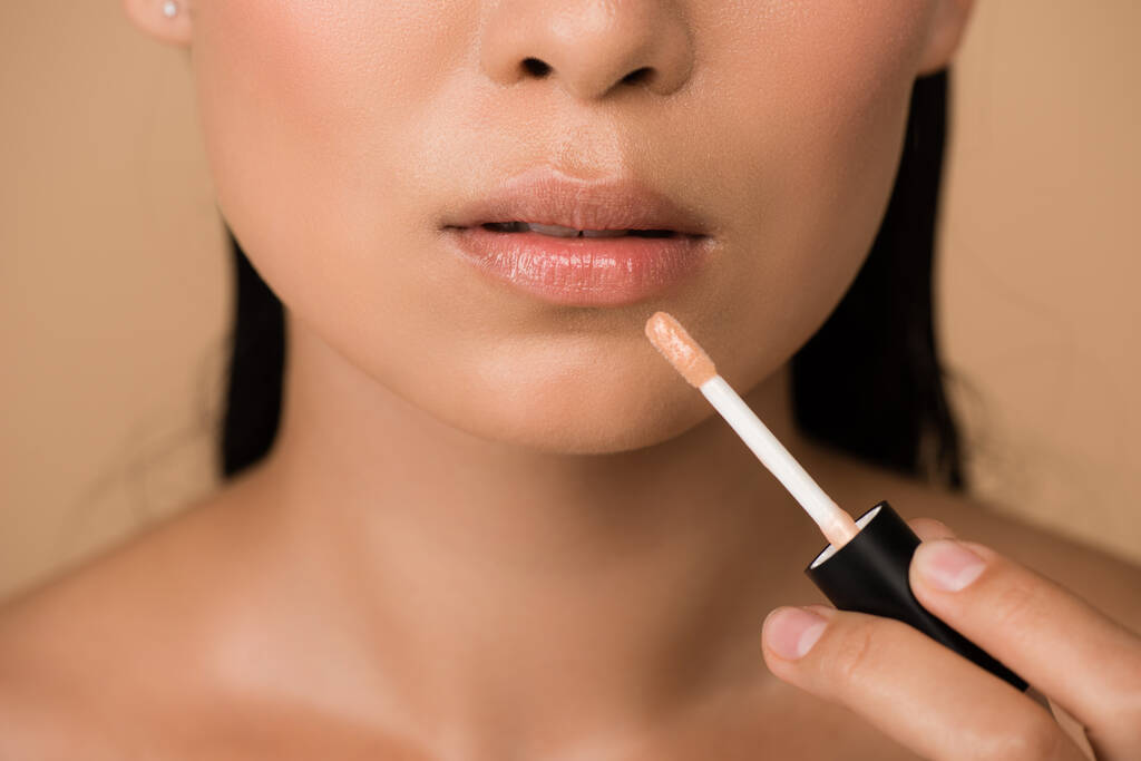cropped view of beautiful naked asian girl appying lip gloss on lips isolated on beige - Photo, Image