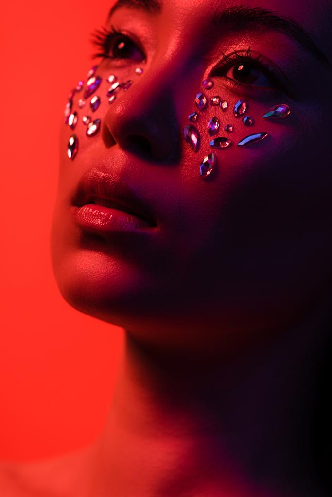 hermosa chica asiática con diamantes de imitación en la cara aislado en rojo
 - Foto, imagen