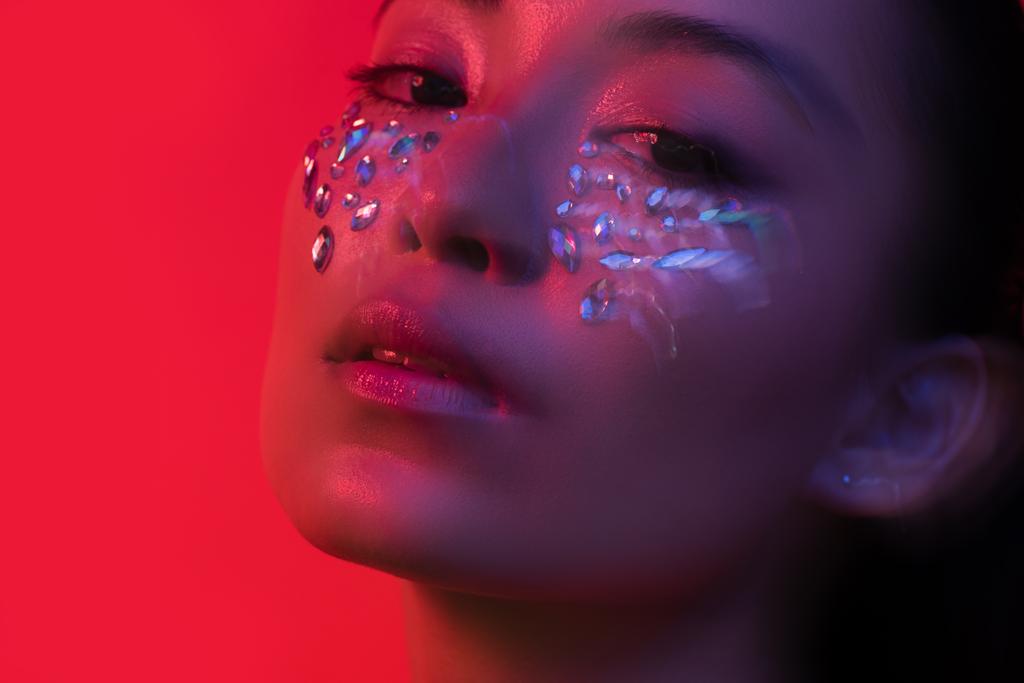 beautiful asian girl with rhinestones on face isolated on red, motion blur - Photo, Image