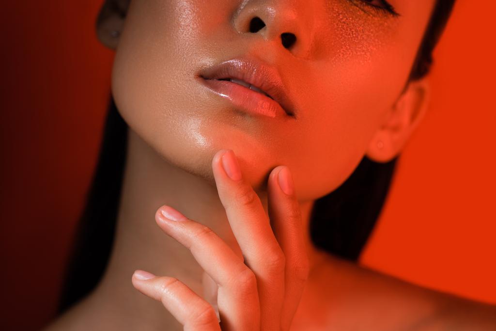 cropped view of beautiful asian girl touching glossy face in red lighting - Photo, Image