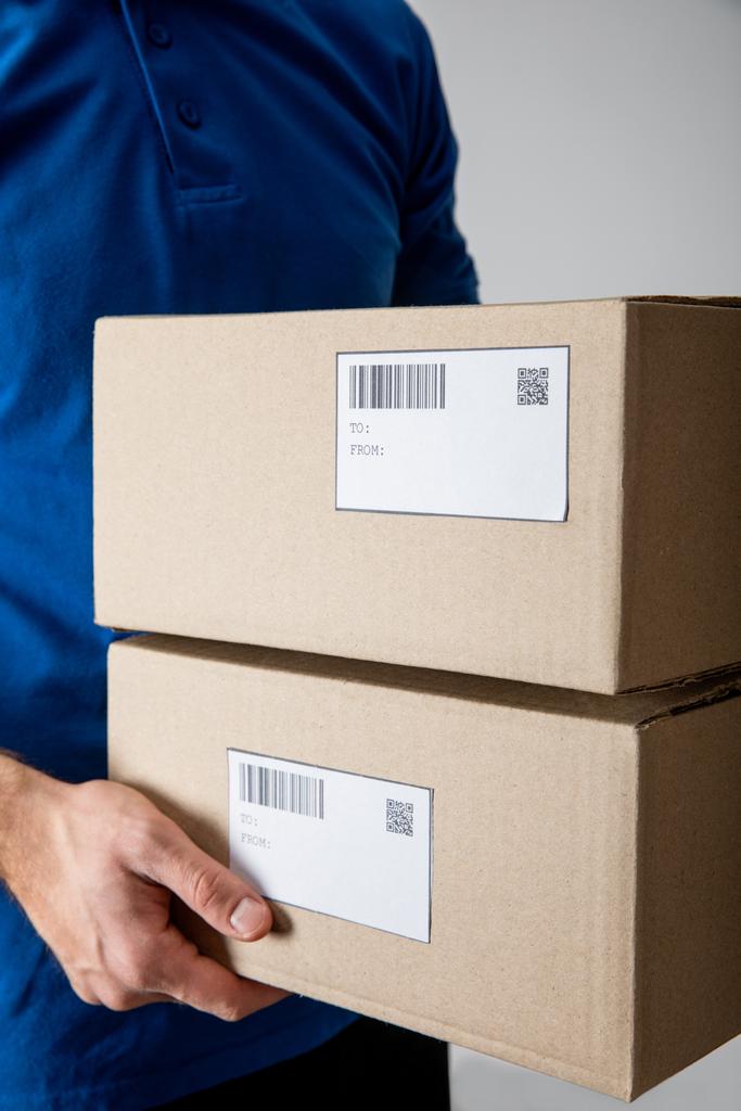 Обрізаний вид доставки людини, що тримає картонні коробки ізольовані на сірому
 - Фото, зображення