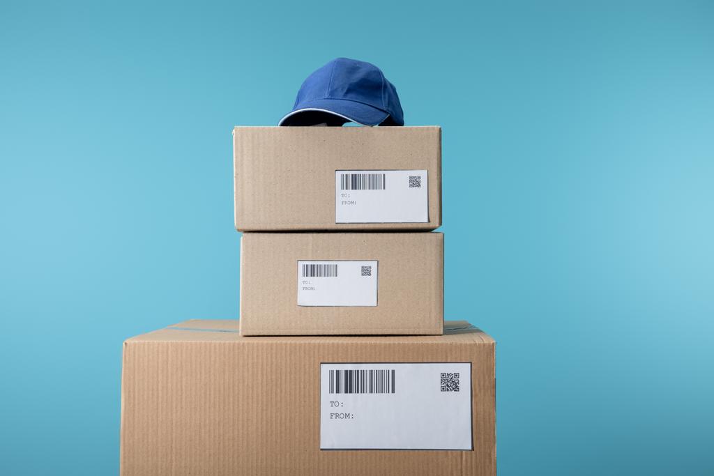 Casquette sur boîtes en carton empilées isolées sur bleu
 - Photo, image