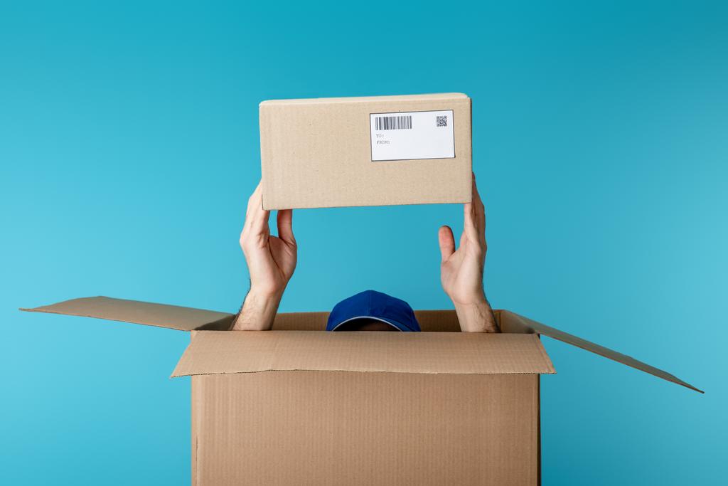 Vista recortada del mensajero en la tapa que sostiene el paquete de cartón de la caja aislada en azul
 - Foto, imagen