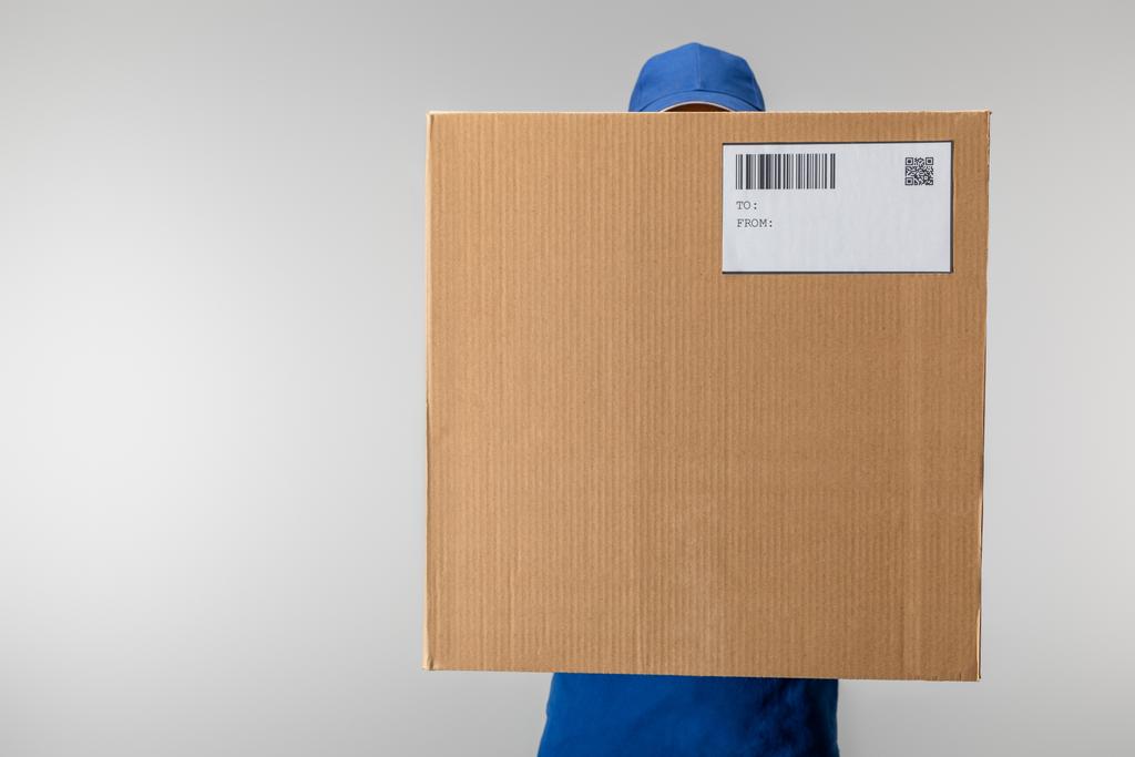 Uomo di consegna in scatola di cartone uniforme con codice qr e codice a barre isolato su grigio
 - Foto, immagini