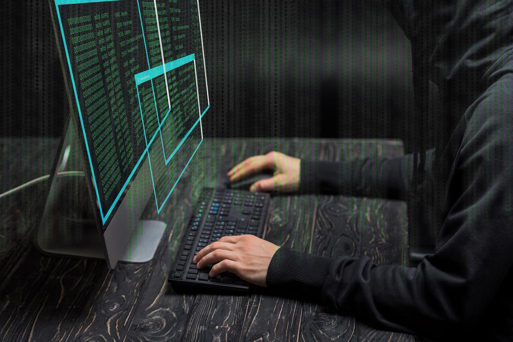 vue recadrée du pirate tapant sur le clavier de l'ordinateur près de l'écran de l'ordinateur avec des données sur noir
  - Photo, image