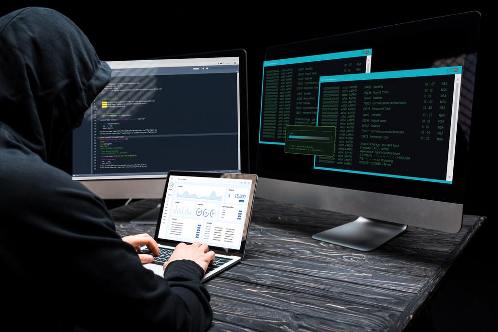 хакер с помощью ноутбука с графиками и графиками на экране рядом с мониторами компьютера на черном
  - Фото, изображение