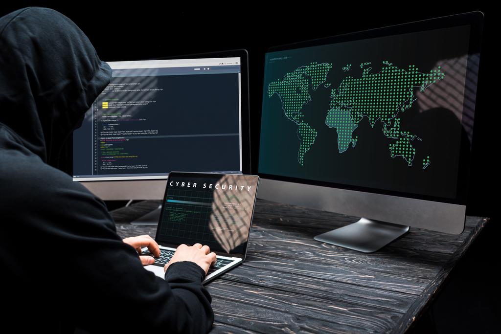хакер с помощью ноутбука с кибер-безопасности надписи на экране рядом с мониторами компьютера на черном
  - Фото, изображение