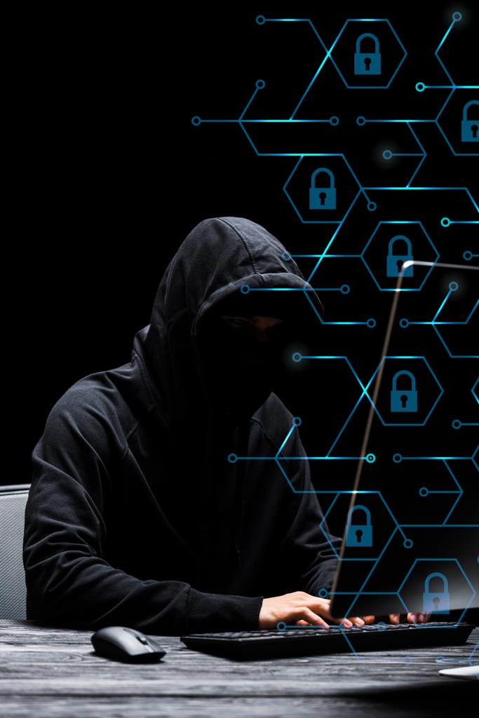 haker w masce siedzi w pobliżu monitora komputerowego i wpisując na klawiaturze komputera w pobliżu kłódek na czarny  - Zdjęcie, obraz
