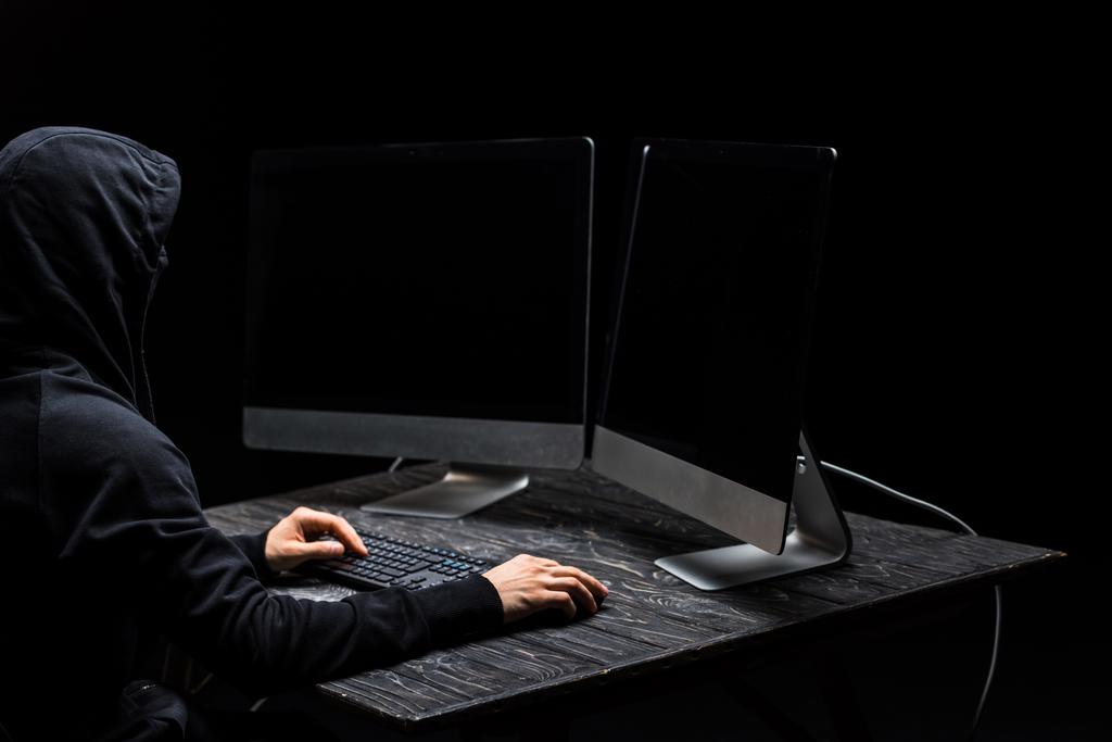 hacker using computer mouse and looking at computer monitors with blank screen isolated on black  - Photo, Image