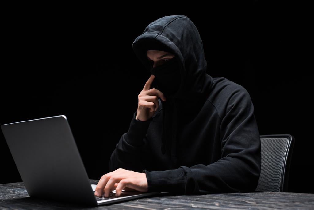 молодой хакер прикосновения маски и с помощью ноутбука изолированы на черный
  - Фото, изображение