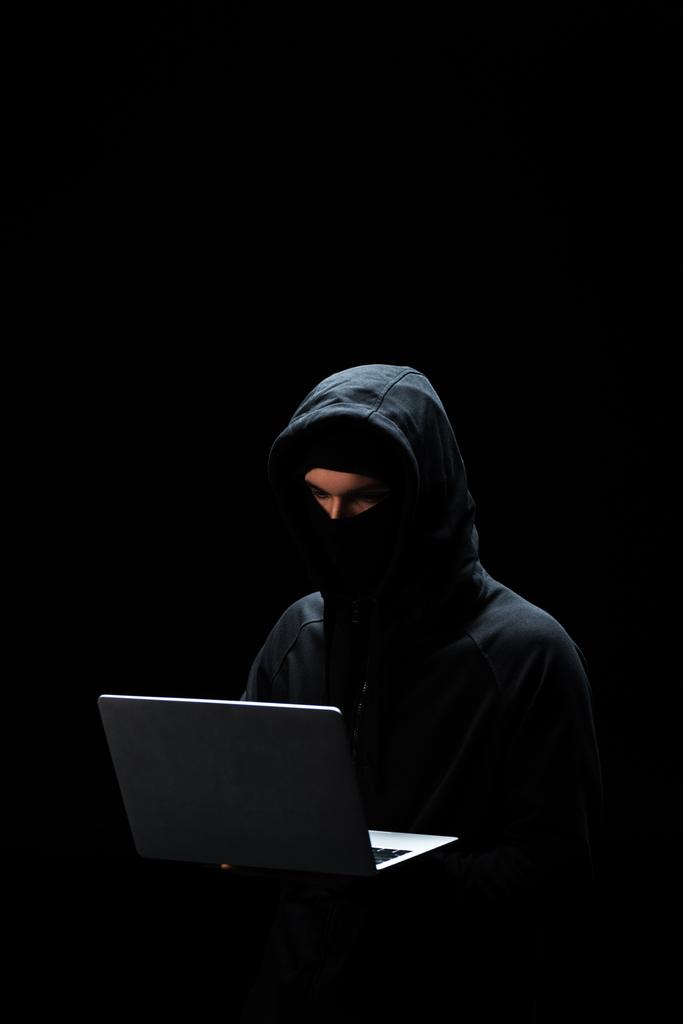 giovane hacker in cappuccio utilizzando laptop isolato su nero
  - Foto, immagini