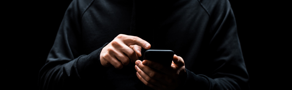 panorámás lövés hacker mutatva ujjal okostelefon elszigetelt fekete  - Fotó, kép