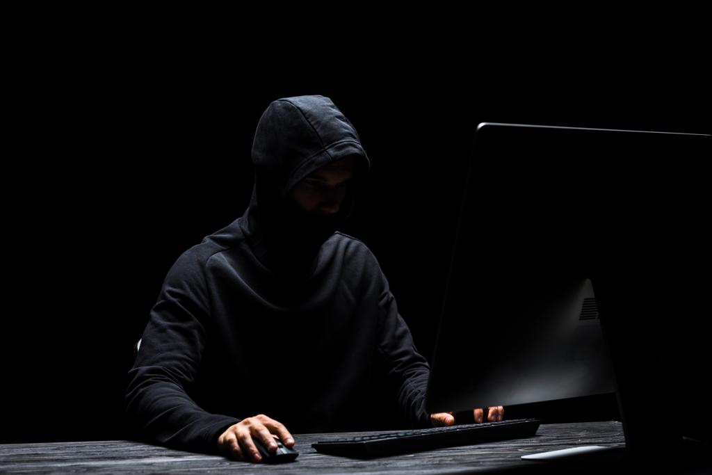 skrytý anonymní hacker v masce pomocí počítače izolovaného na černém  - Fotografie, Obrázek