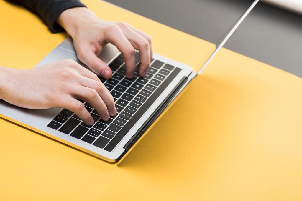oříznutý pohled hackera pomocí notebooku na žlutém stole  - Fotografie, Obrázek