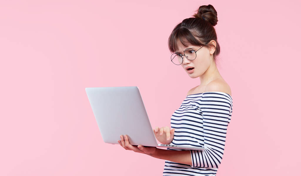 Choqué inquiet jeune asiatique femelle bureau assistant dans les lunettes tenir ordinateur portable, stand rose fond
 - Photo, image