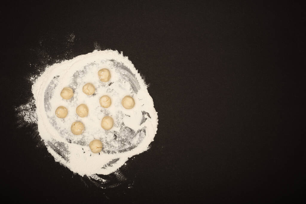 top view of raw dough balls for dumplings on flour on black background - Fotoğraf, Görsel