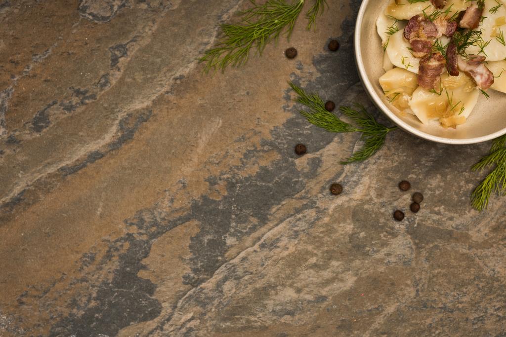 vista superior de la deliciosa varenyky con crujientes en un tazón cerca de eneldo y granos de pimienta negra en la superficie de piedra
 - Foto, Imagen