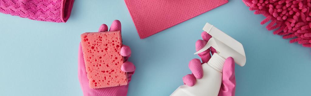 panoramisch schot van huishoudster in roze rubberen handschoenen met spons en spuitfles op blauw met vodden - Foto, afbeelding