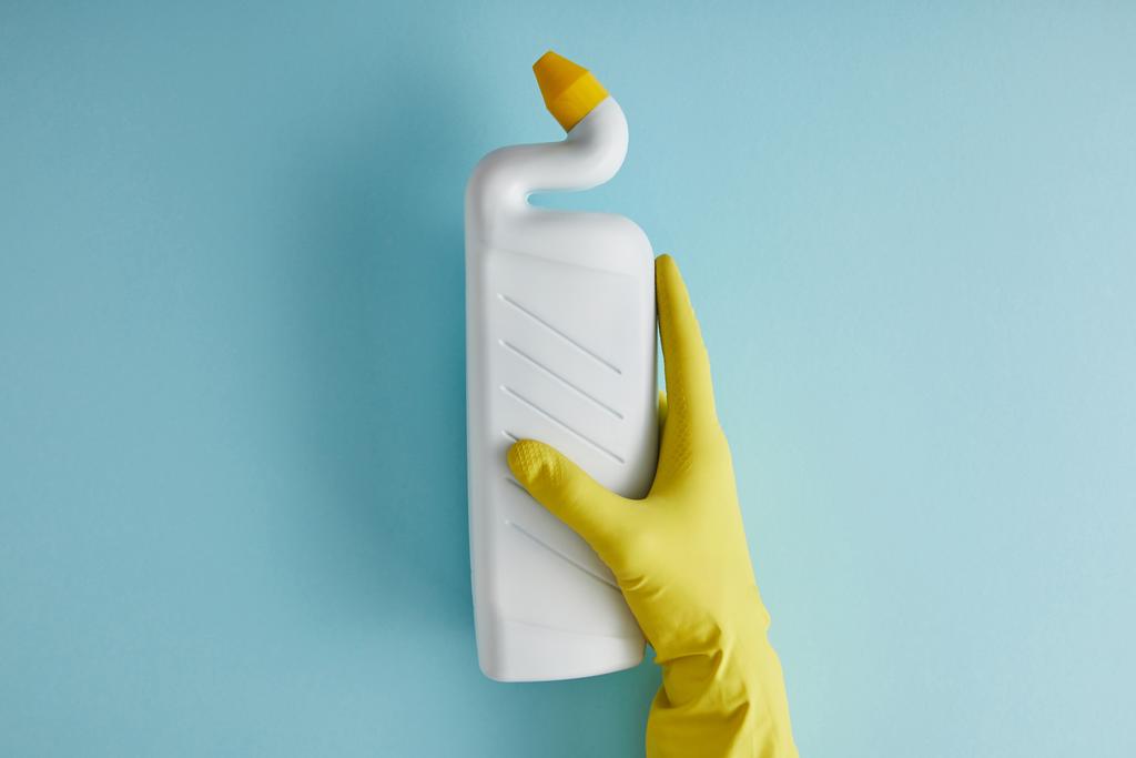 bijgesneden mening van huishoudster in rubber handschoen holding fles met toilet reiniger op blauw - Foto, afbeelding