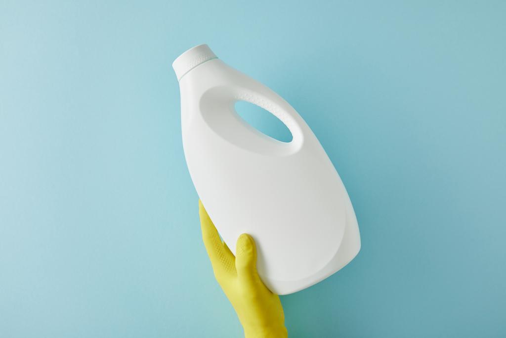 καλλιεργημένη άποψη της οικονόμου σε πλαστικό γάντι κρατώντας μπουκάλι με προϊόν καθαρισμού σε μπλε - Φωτογραφία, εικόνα