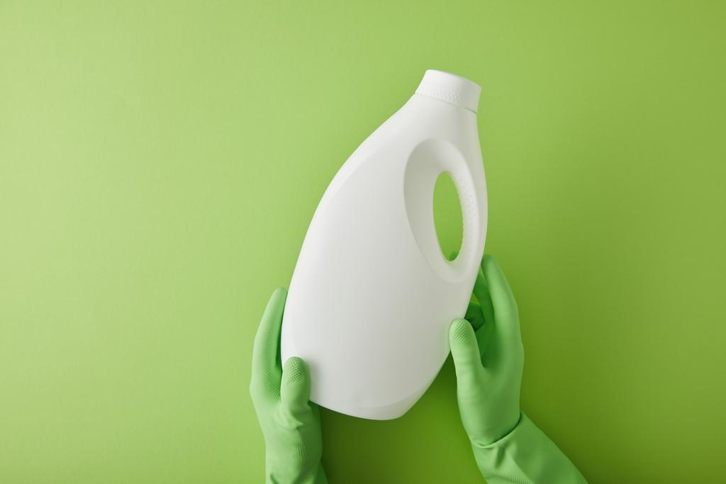 вид зверху домогосподарки в гумових рукавичках, що тримає пляшку з прибиральником на зеленому
  - Фото, зображення