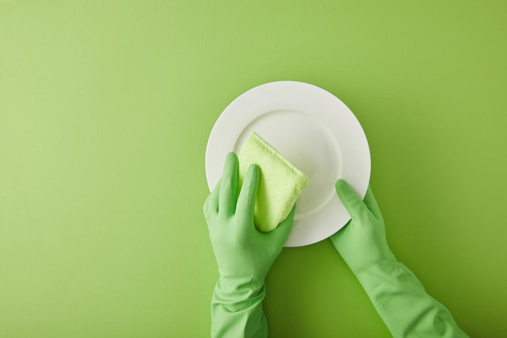 обрізаний вид домогосподарки в гумових рукавичках пральна пластина з губкою на зеленому
  - Фото, зображення