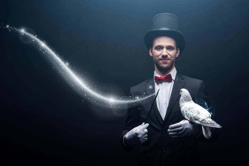 happy magician in hat making abracadabra with dove and wand in dark room with smoke and glowing illustration - Photo, Image