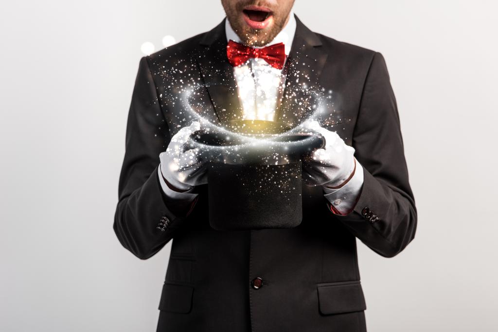 cropped view of shocked magician holding hat isolated on grey with glowing illustration - Photo, Image