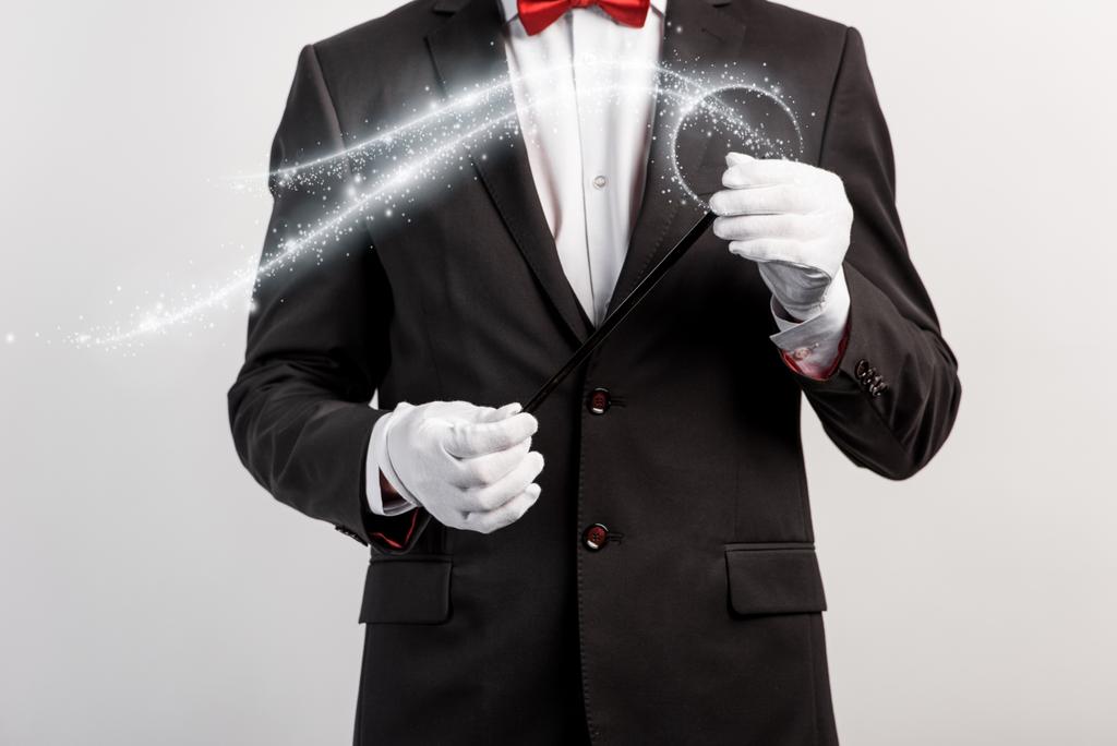 cropped view of magician in suit and hat holding wand isolated on grey with glowing illustration - Photo, Image