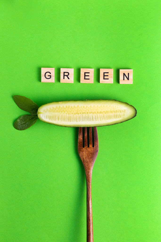 Lettere vegan vegan più sano cetriolo eco su una forchetta di legno su uno sfondo verde
 - Foto, immagini
