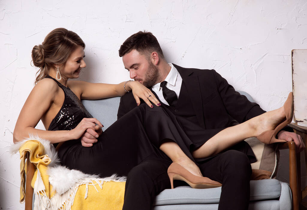 Мужчина целует руки смеющейся девушки, счастливая пара сидит на диване
 - Фото, изображение