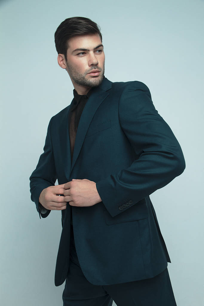 muskulös starkes schönes männliches Modell im formalen blauen Anzug mit Emotionen auf grauem, isoliertem Schriftgrund mit Schatten - Foto, Bild