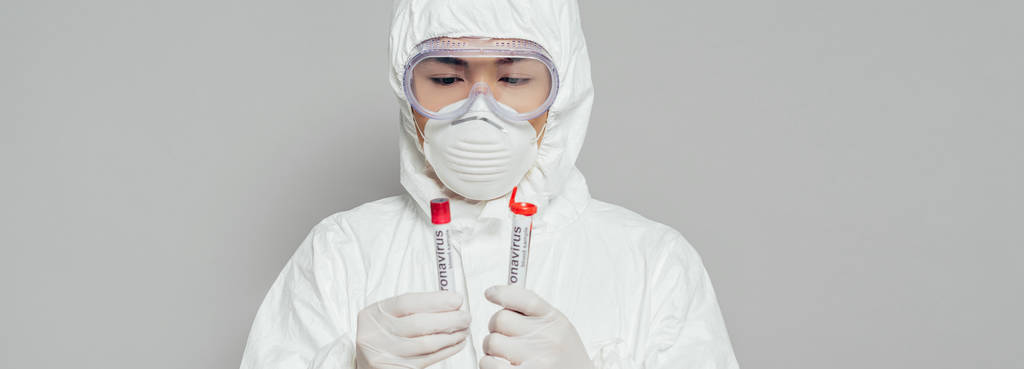 Asyalı epidemiyolojistin tehlikeli madde giysisi ve solunum maskesi içinde kan örnekleri içeren test tüpleri tutarken görüntüsü gri renkte. - Fotoğraf, Görsel