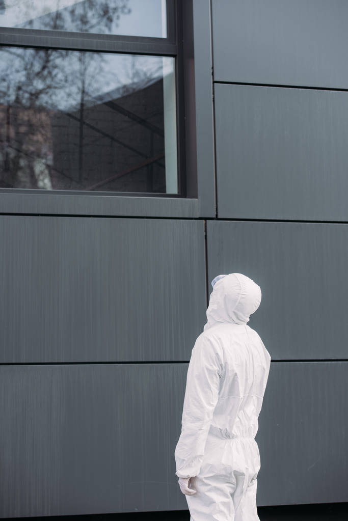 takana näkymä epidemiologi hazmat puku seisoo ulkona ja katselee ikkunasta rakennuksen
 - Valokuva, kuva