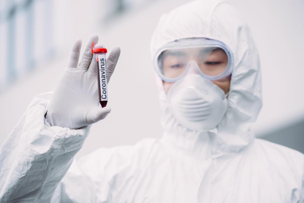 ásia epidemiologista no hazmat terno e respirador máscara olhando para teste tubo com sangue amostra enquanto em pé ao ar livre
 - Foto, Imagem