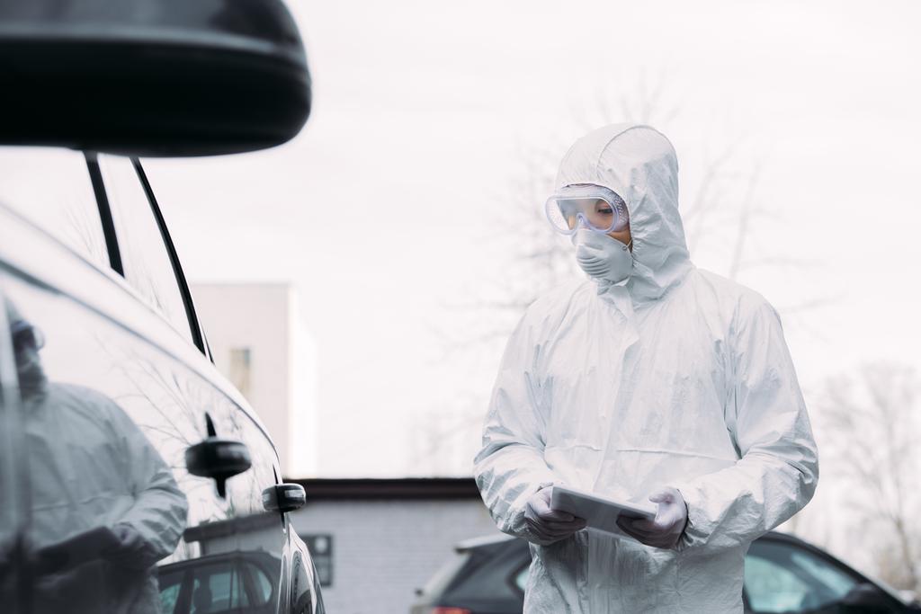 szelektív fókusz ázsiai epidemiológus vegyvédelmi ruha és légzőkészülék maszk gazdaság digitális tabletta, miközben vizsgálja járművek utcai  - Fotó, kép