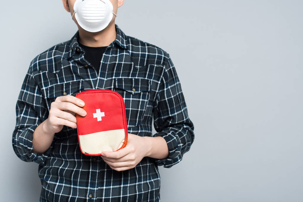 vista recortada del hombre en máscara respiratoria que muestra botiquín de primeros auxilios aislado en gris
 - Foto, imagen