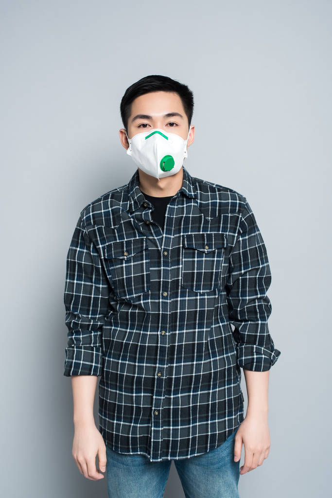 νεαρός ασιάτης με μάσκα αναπνοής κοιτάζει την κάμερα ενώ στέκεται σε γκρι φόντο - Φωτογραφία, εικόνα