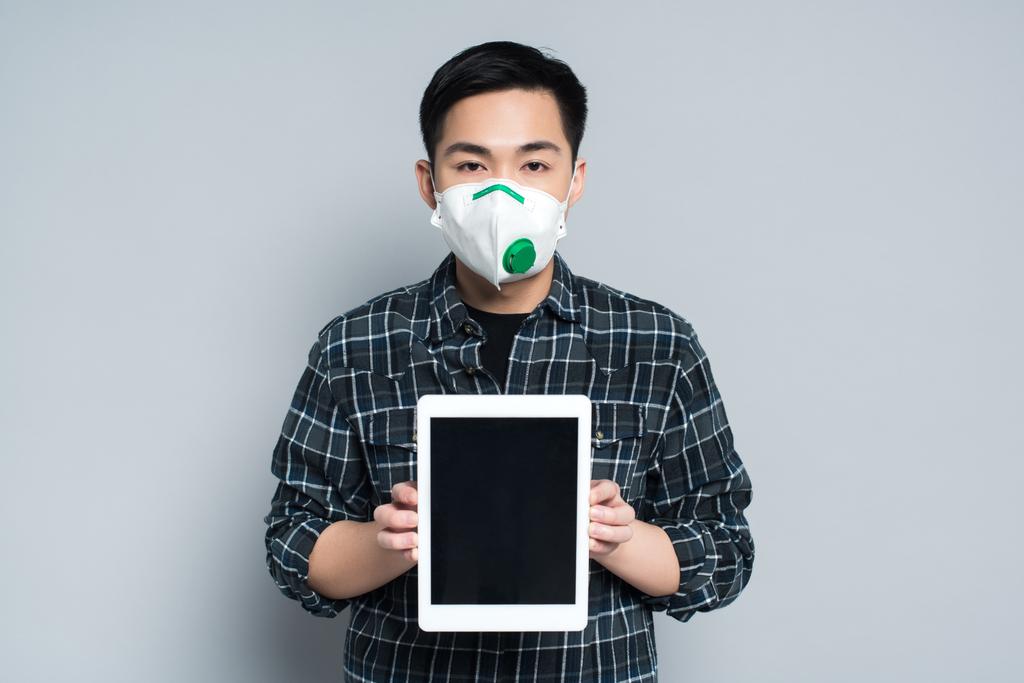 jovem asiático homem no respirador máscara mostrando digital tablet com branco tela no cinza fundo
 - Foto, Imagem