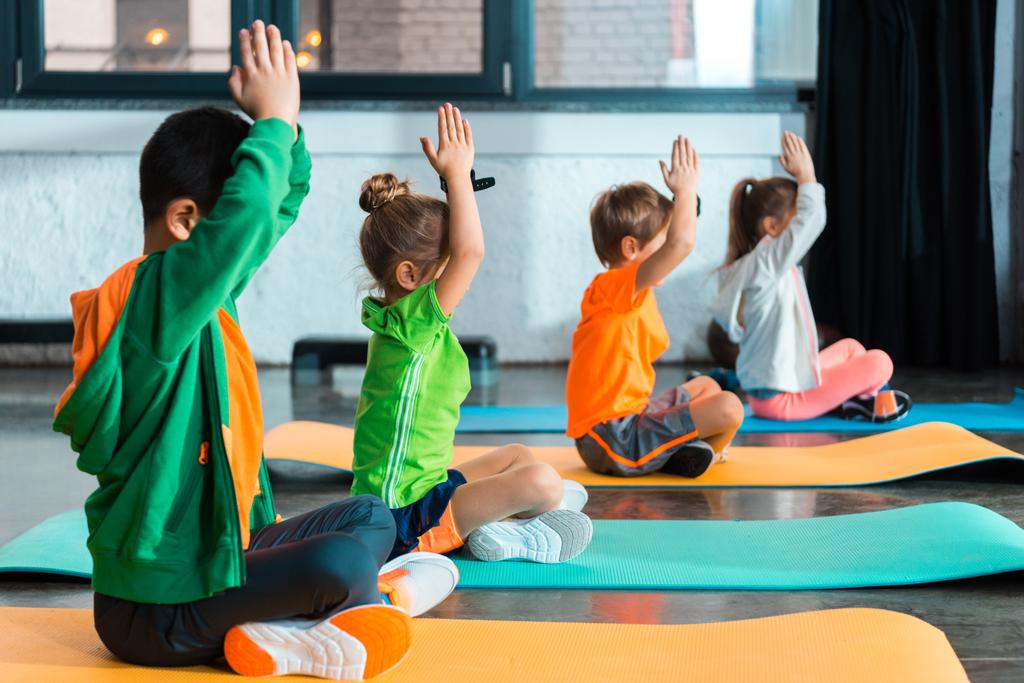 Selectieve focus van kinderen met gebalde handen die zich uitstrekken op fitnessmatten in de fitnessruimte - Foto, afbeelding
